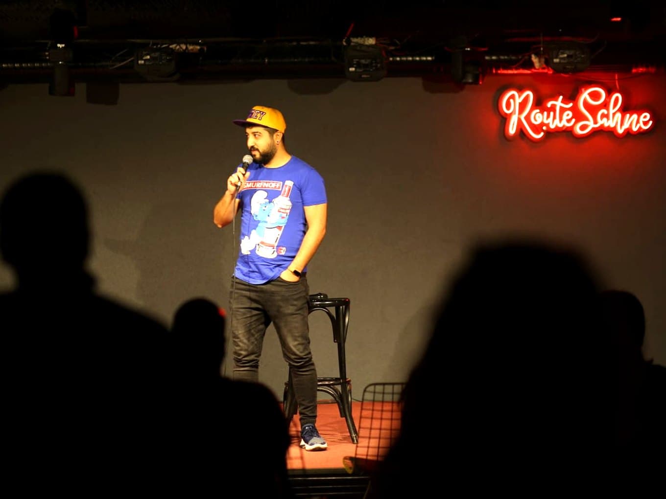 İbrahim Sencer Özer on stage with a microphone, Route Sahne neon sign behind him